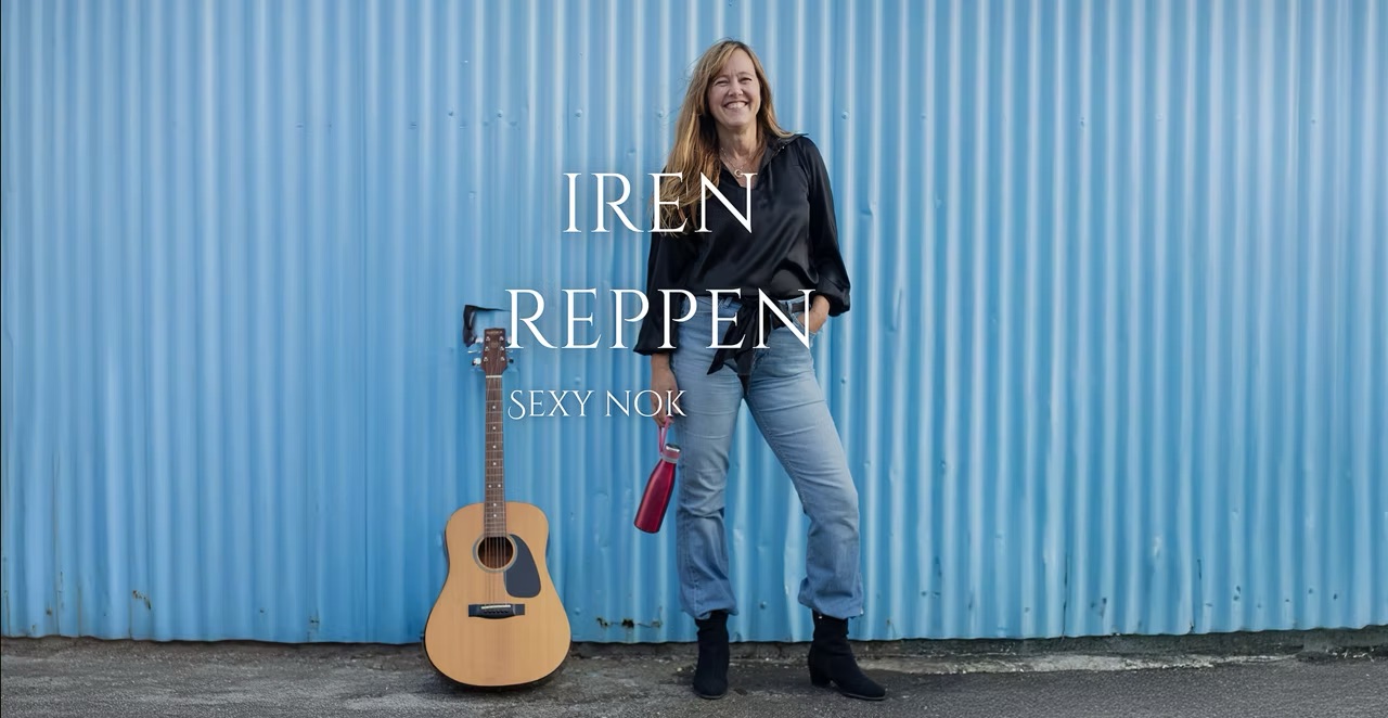 Kvinne med gitar som står foran en blå vegg